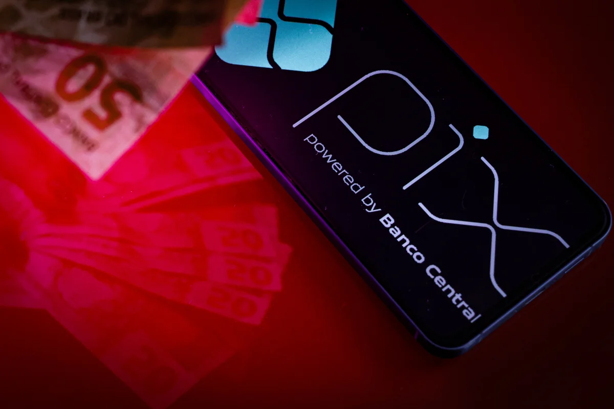 Imagem colorida mão com dinheiro e aplicativo PIx dinheiro pagamento moeda digital - Metrópoles