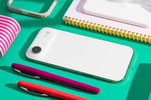 A white iPhone Air resting on a teal surface alongside a notebook and two pens.