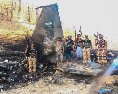 Houthi fighters pose amid the wreckage of a downed and blackened shell of a fighter jet