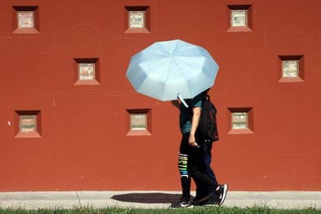 Two people walk sharing a large pale blue umbrella during a heat warning in Los Angeles