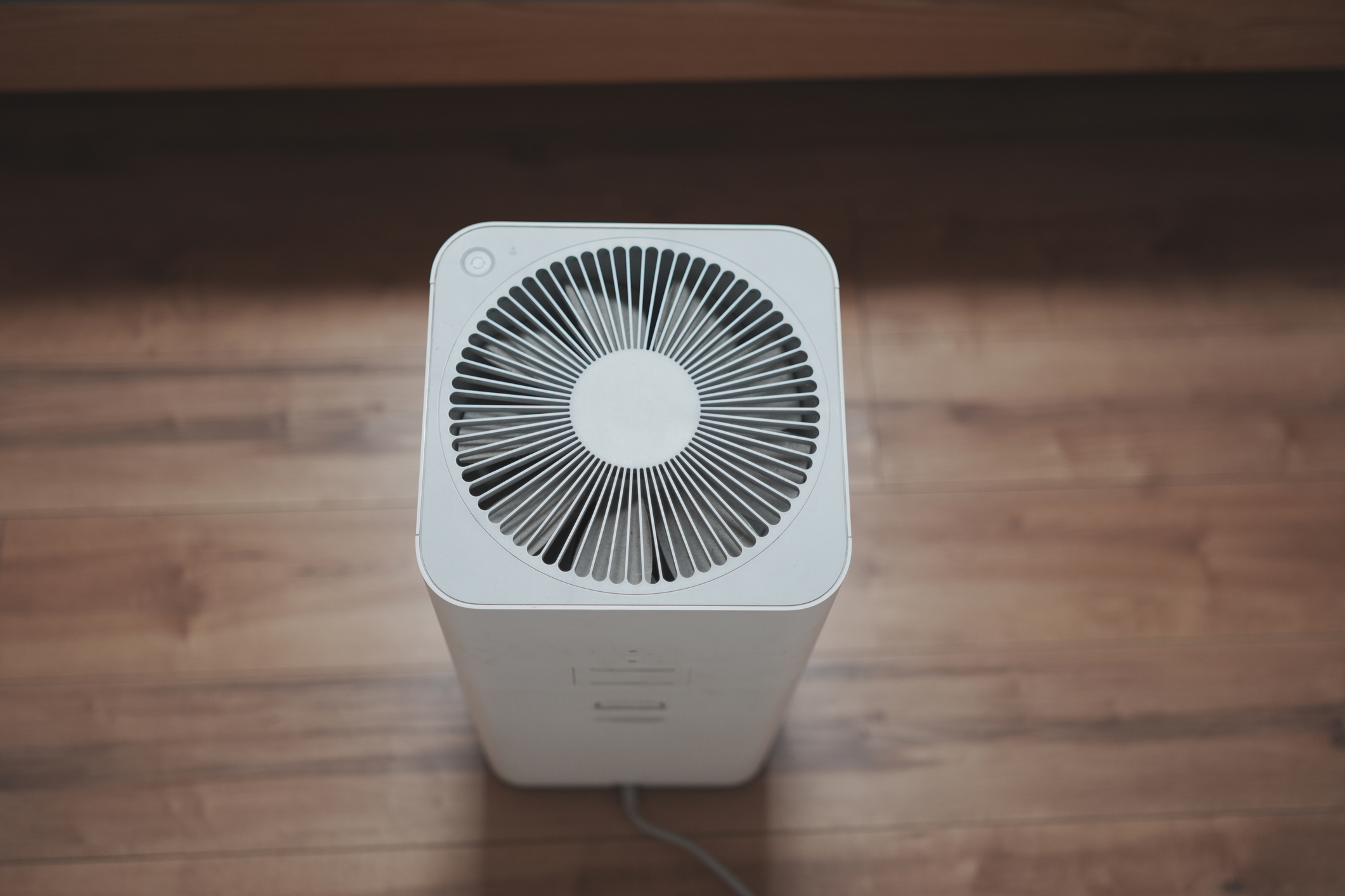 The top of a white air purifier on a wood floor.