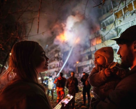 A family looks on as a Kyiv building hit by a missile strike burns behind them.