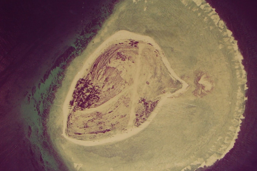 An image of a barren island from the air, showing the coral reef surrounding it.