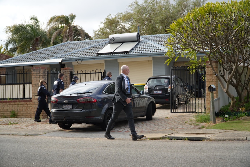 Several police officers including a detective walk outside a residential home.
